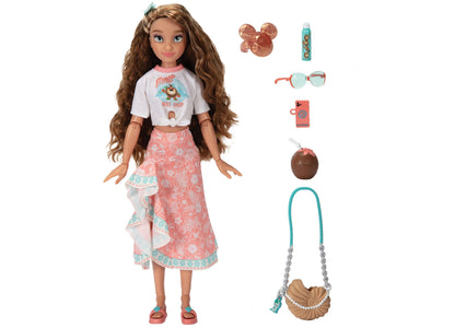 Moana fashion doll with long brown wavy hair wearing white surf shop graphic tee and coral patterned skirt, modeled by a child, shown with accessories including