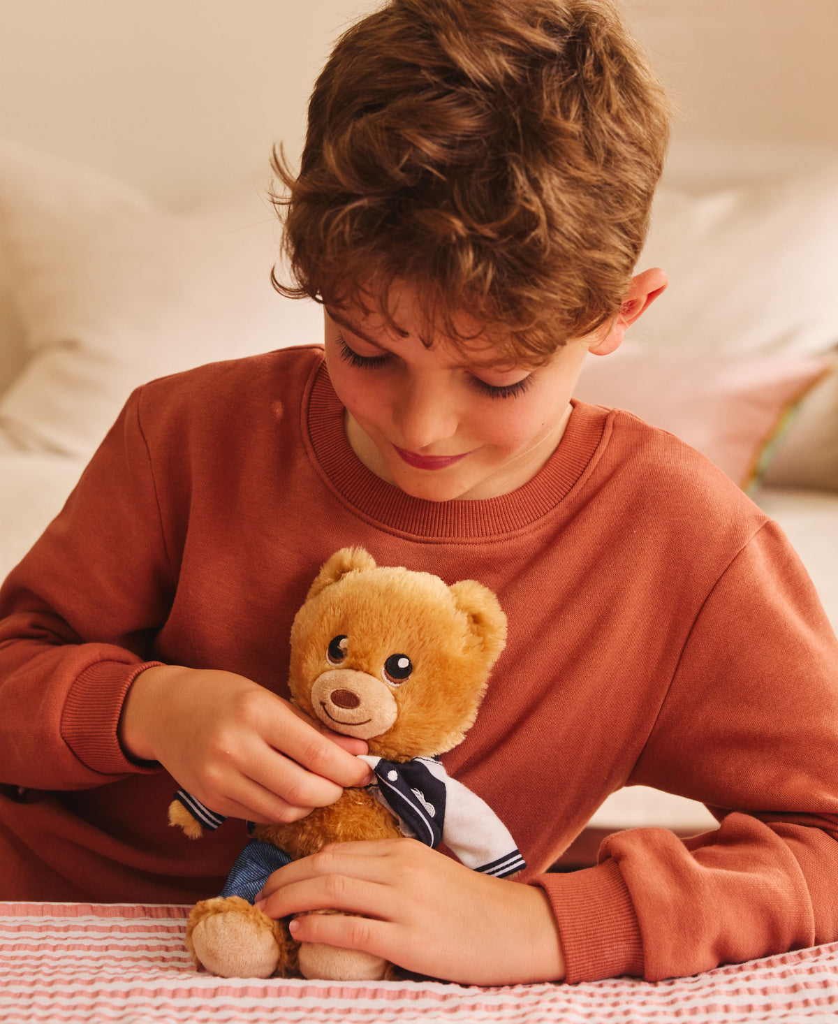 Child in rust sweatshirt dressing tan teddy bear with navy and white outfit at Casdon Build-A-Bear Workshop Stuffing ...