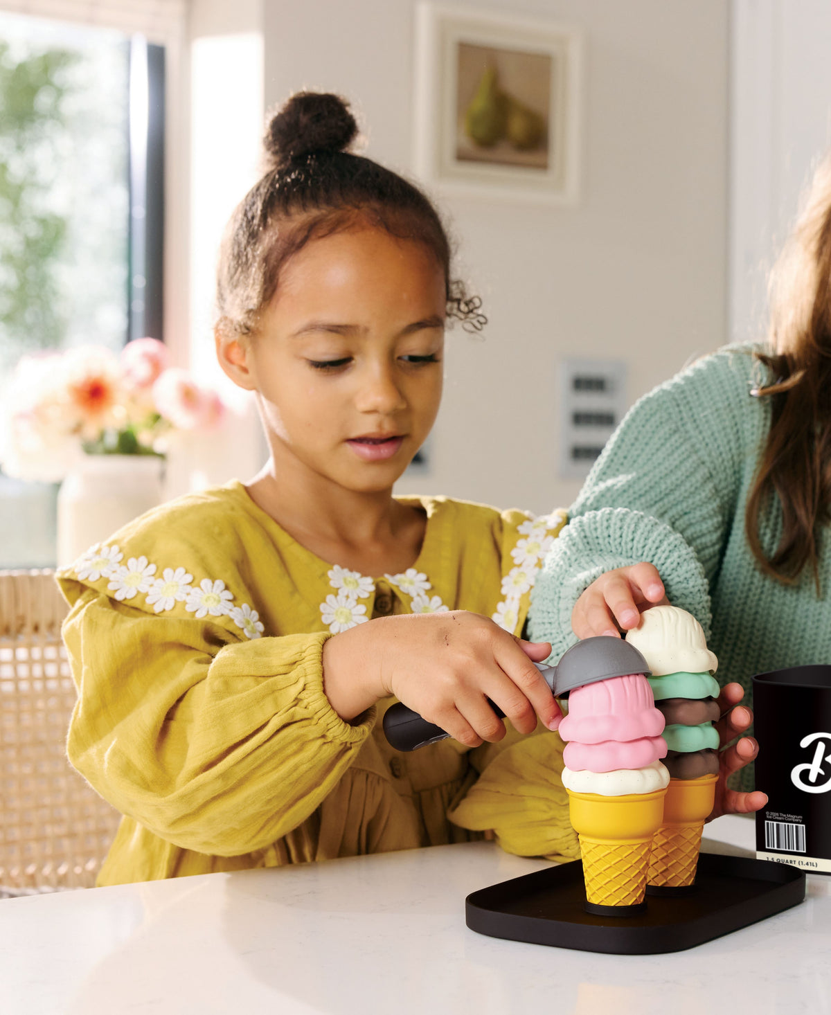 Child in yellow shirt stacking colorful ice cream scoops on cone with Casdon Breyers playset