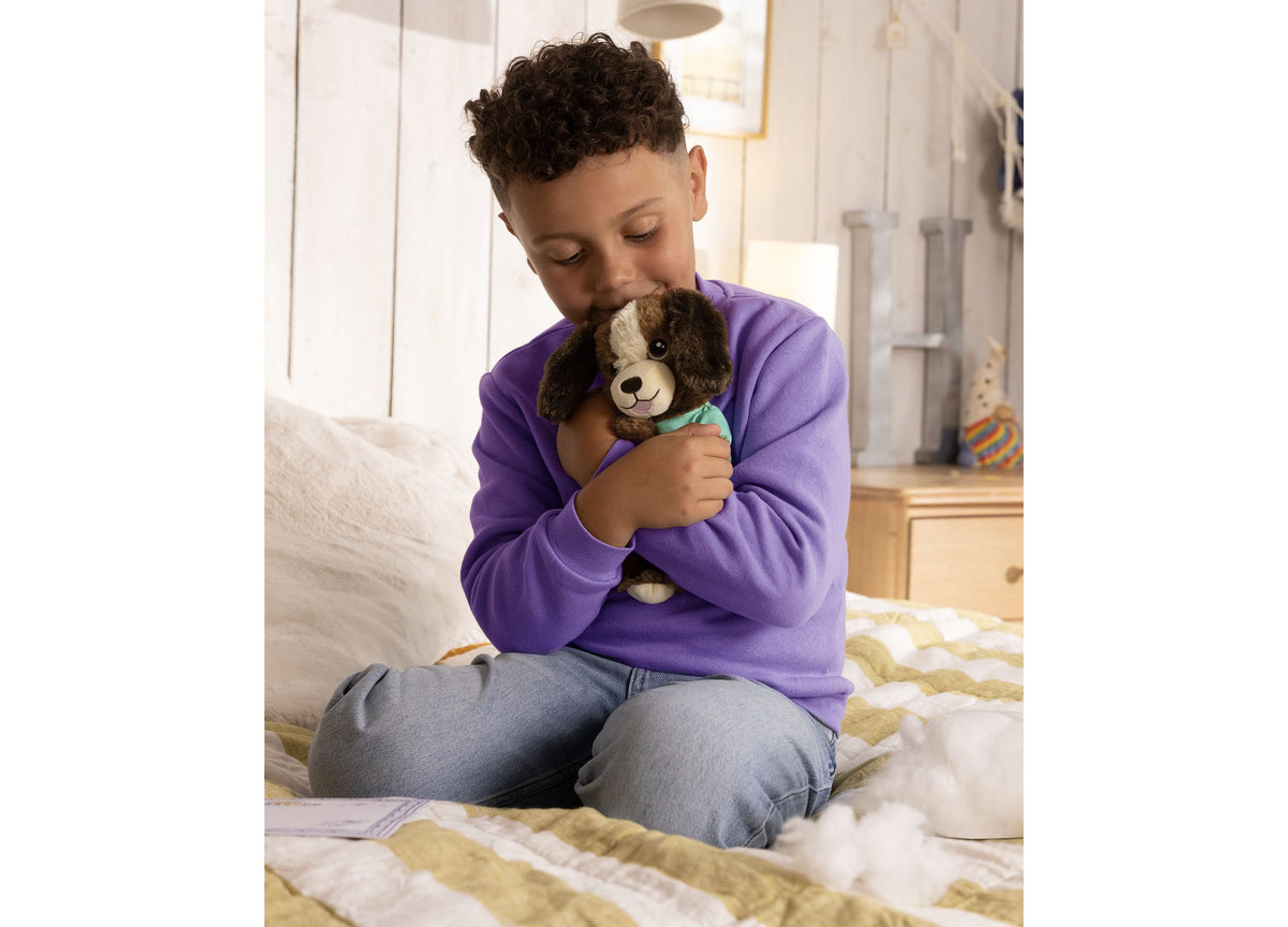 Child in purple shirt holding brown and white puppy toy with turquoise collar on bed