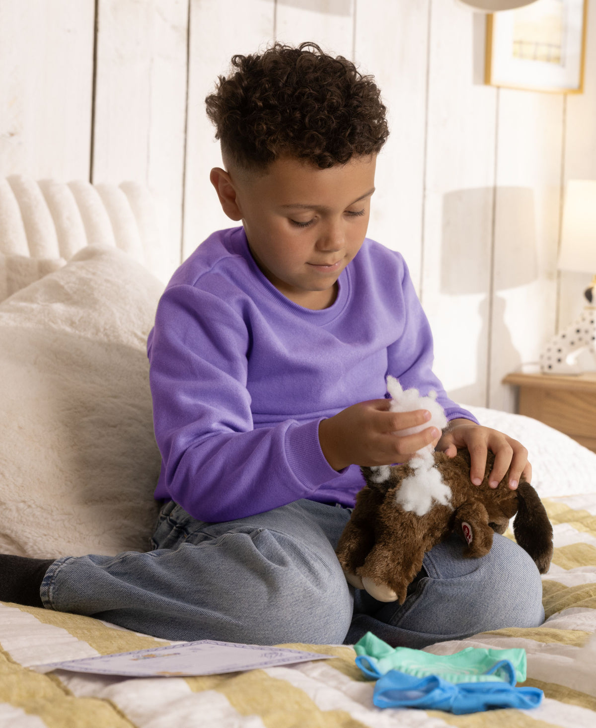 Child in purple shirt dressing brown puppy toy with white heart patch and accessories