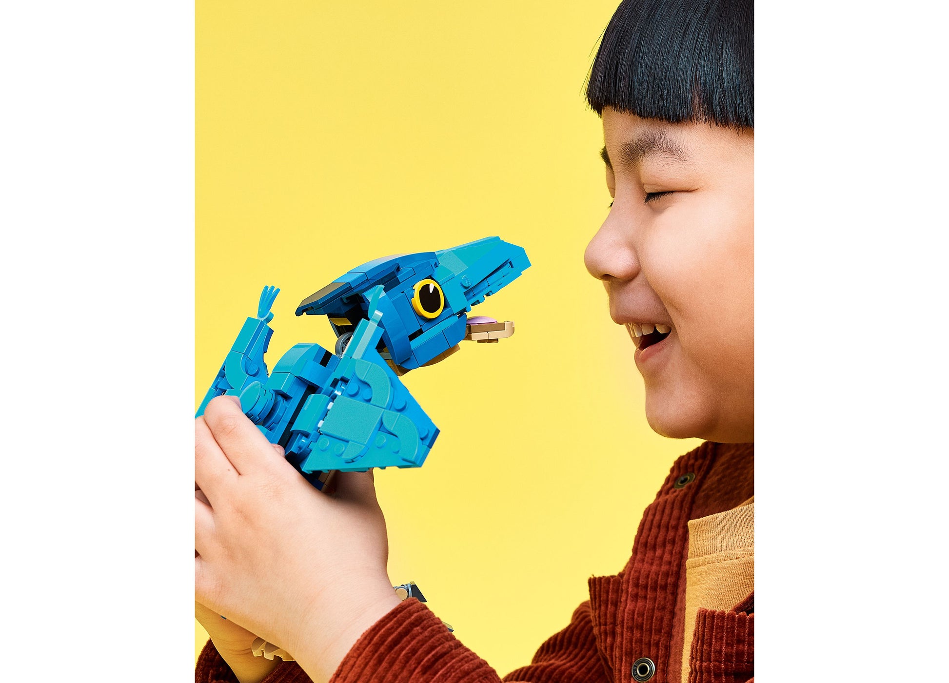 Child holding blue LEGO Jurassic World Pteranodon dinosaur toy set against yellow background