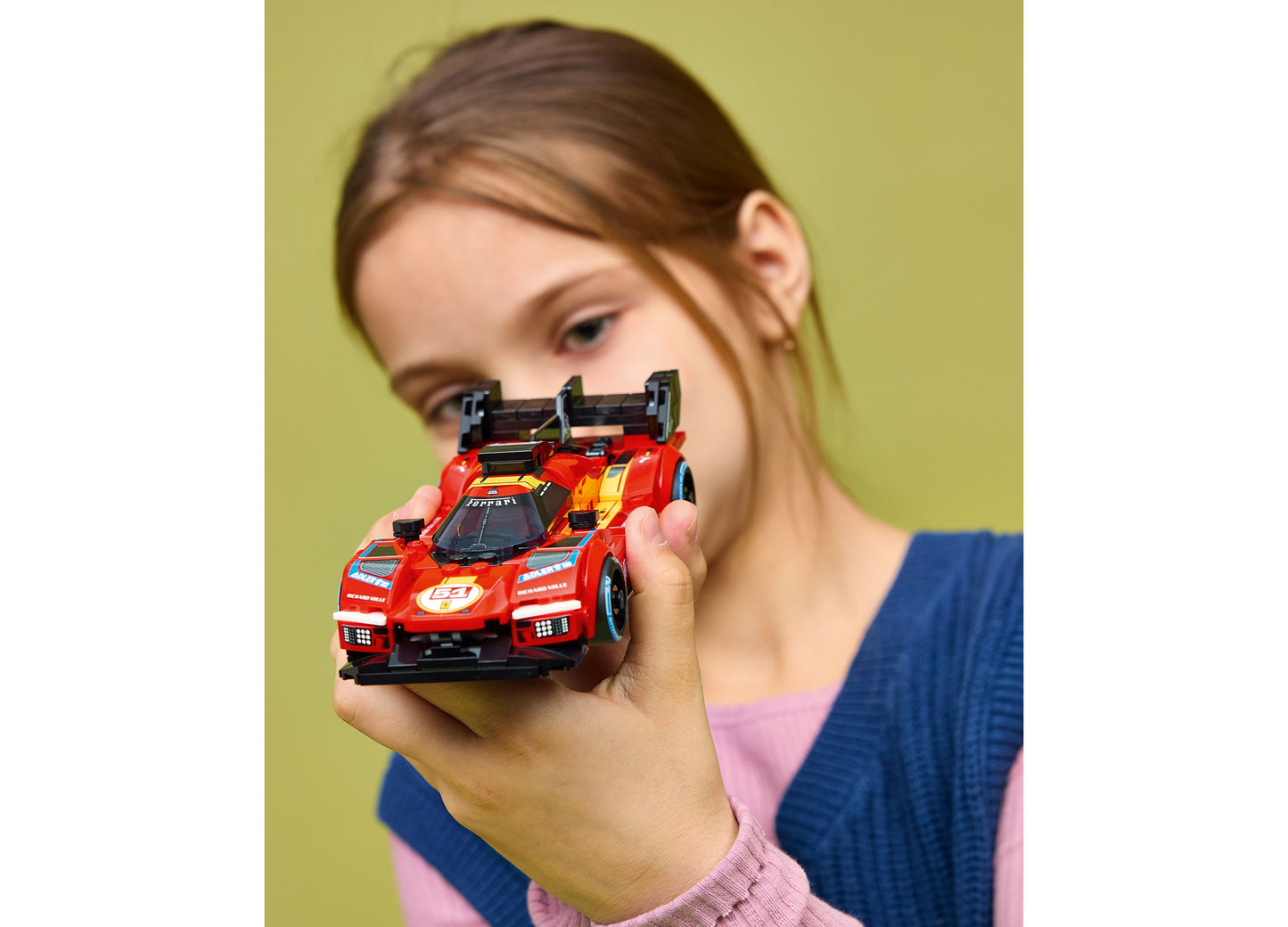 Child holding red LEGO Speed Champions Ferrari 499P building set against yellow background
