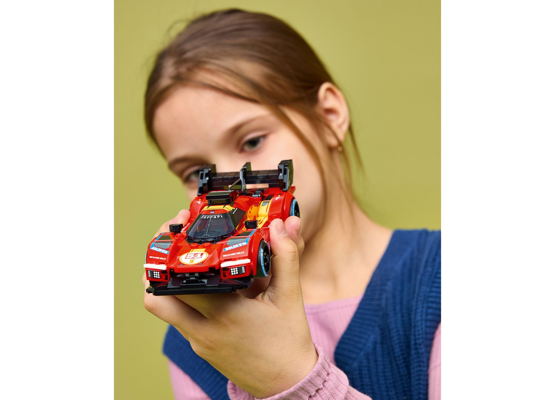 Child holding red LEGO Speed Champions Ferrari 499P building set against yellow background