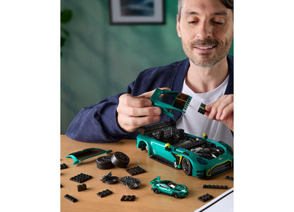 Man assembling turquoise Hot Wheels Aston Martin Vantage GT3 building set with engine details, removable hood, and in...