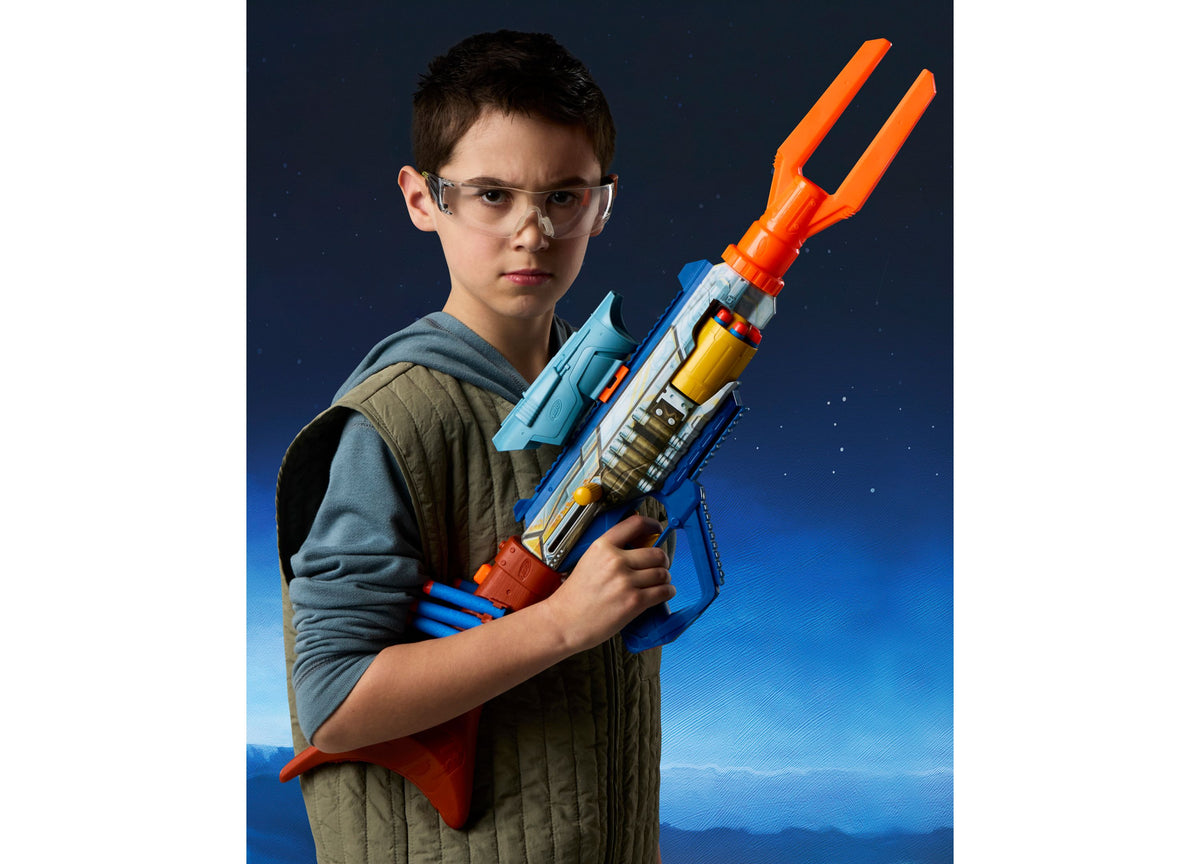 Boy wearing safety glasses holds blue, orange and yellow Nerf Star Wars Mandalorian Bolt-Action Blaster against blue ...