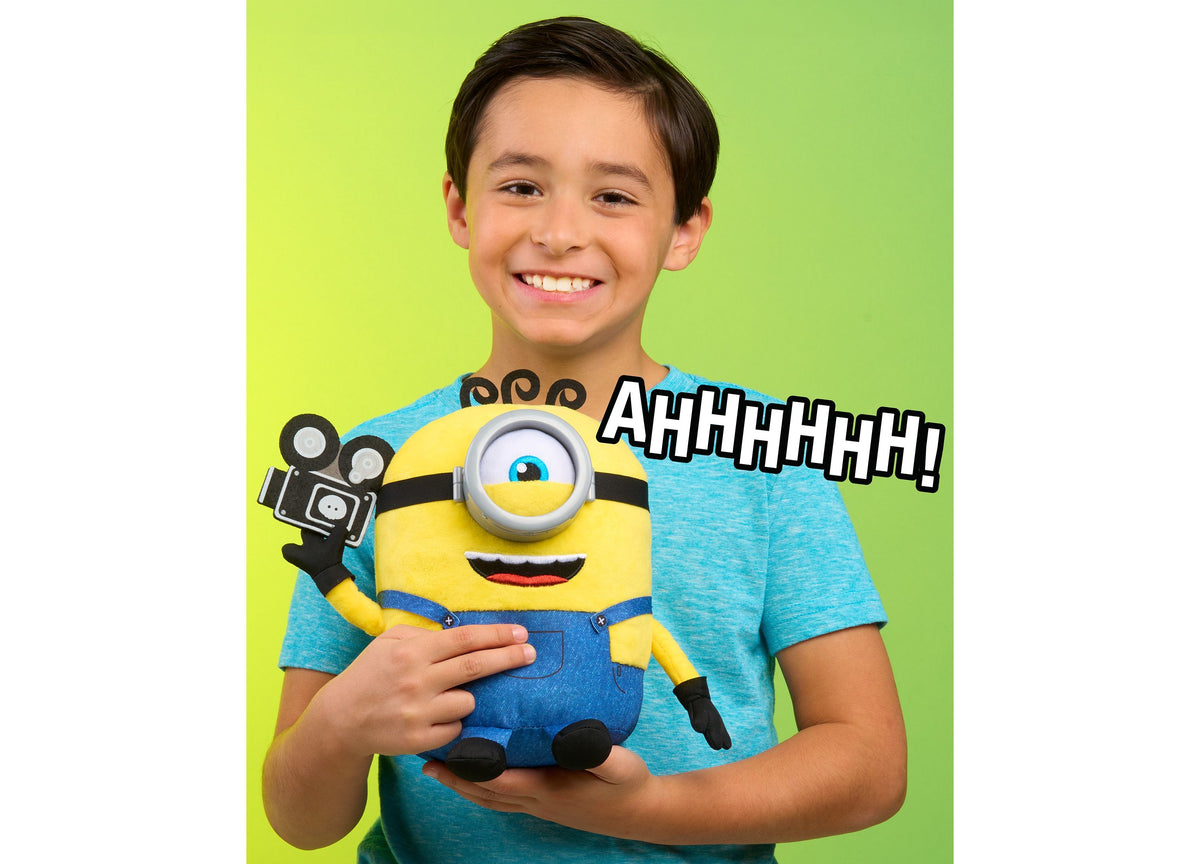 Boy holding yellow Minions James plush toy with camera accessory on lime green background