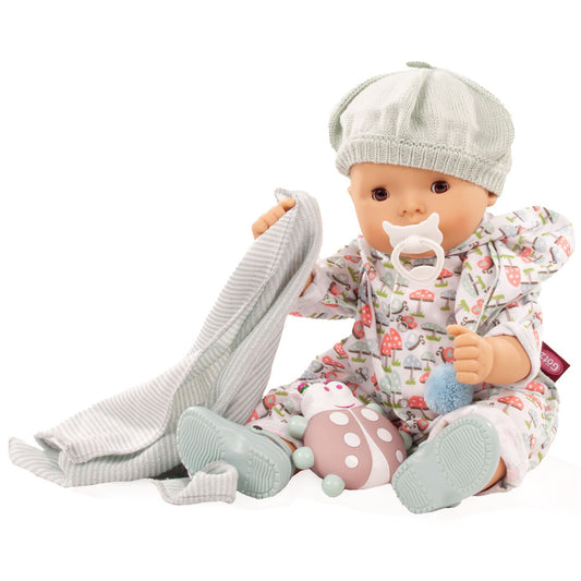 Baby doll wearing white knit hat and mushroom-print outfit with white pacifier, holding gray knit blanket and pink mushroom rattle toy
