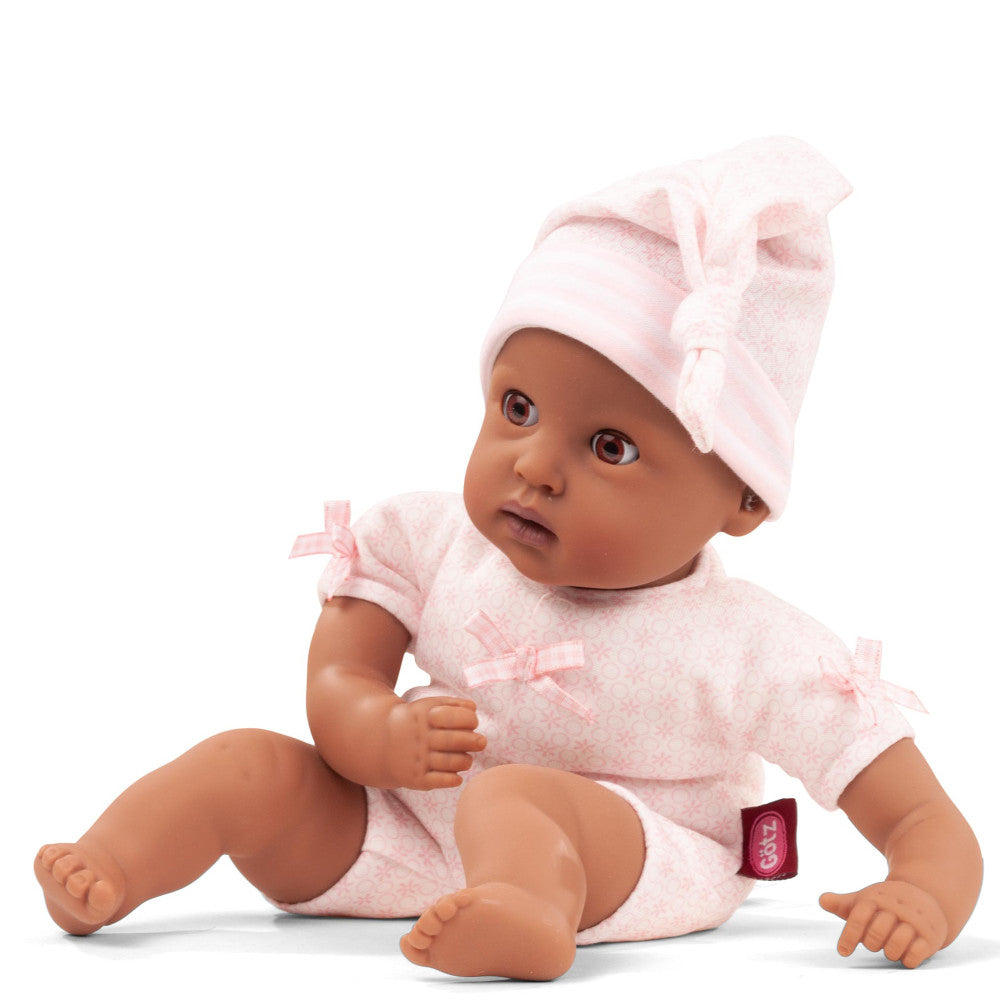 Baby doll with brown skin wearing pink quilted romper and matching bonnet with bow, sitting on plain background
