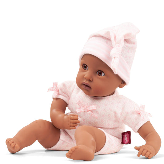 Baby doll with brown skin wearing pink quilted romper and matching bonnet with bow, sitting on plain background