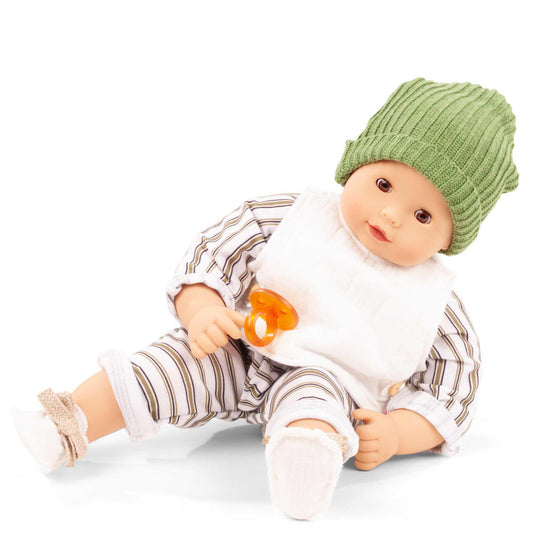 Baby doll wearing green ribbed beanie, white shirt, and striped pants with white socks, holding orange pacifier on plain background