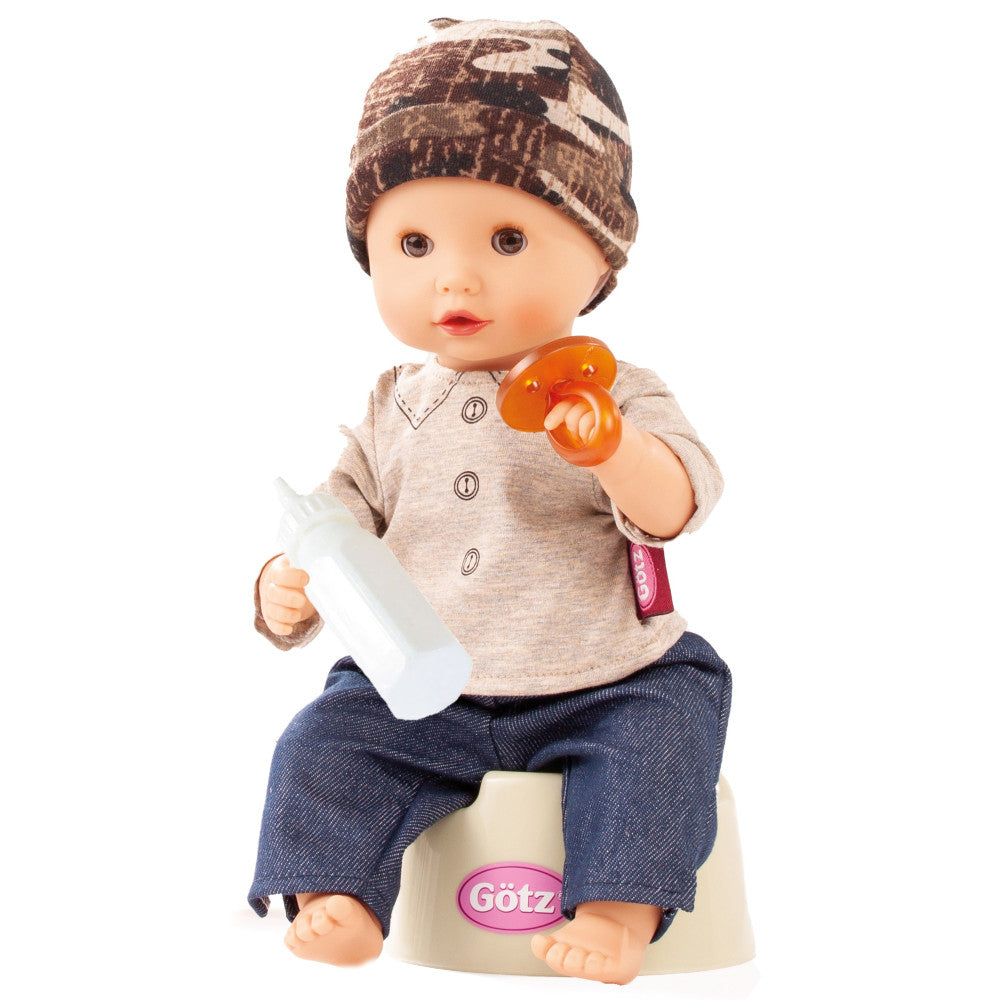 Baby doll wearing brown patterned beanie, beige button-up shirt, and blue pants, holding orange pacifier and white bottle, sitting on cream-colored potty with p