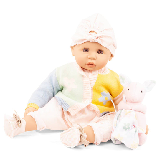 Soft baby doll with open eyes wearing pink headwrap, colorful pastel sweater with star detail, and pink pants, seated with plush accessories on white background