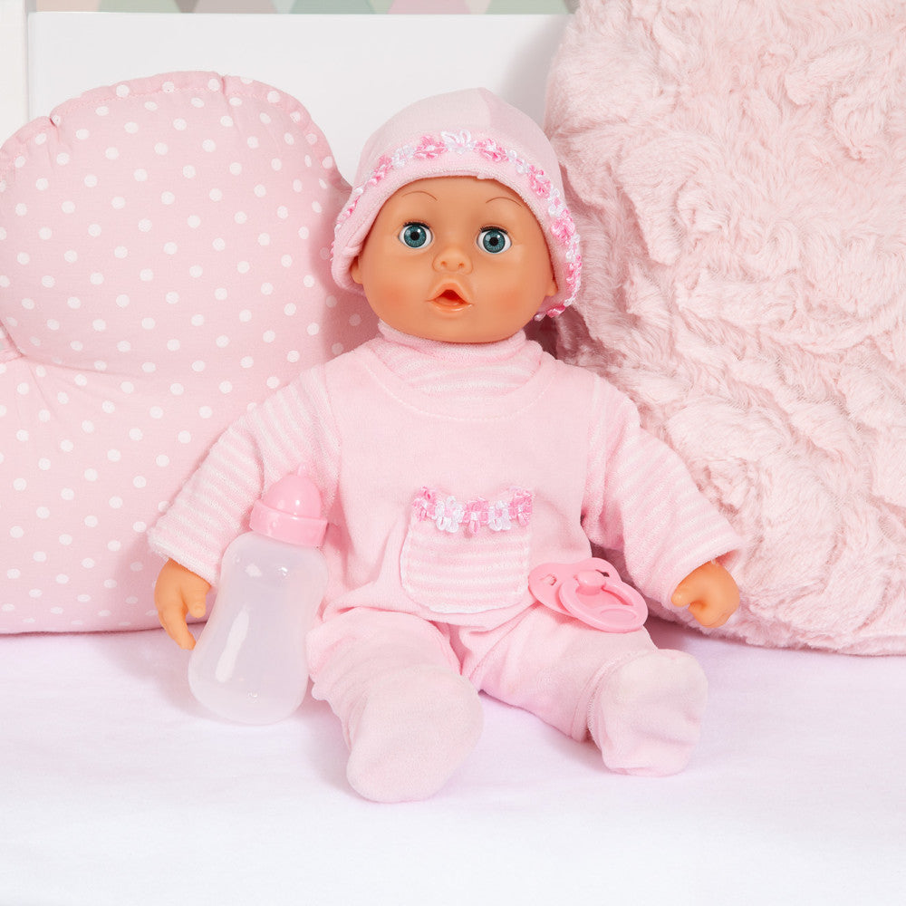 Pink baby doll wearing polka-dot bonnet and pink outfit with white bottle and pacifier, surrounded by pink textured blanket and pillow