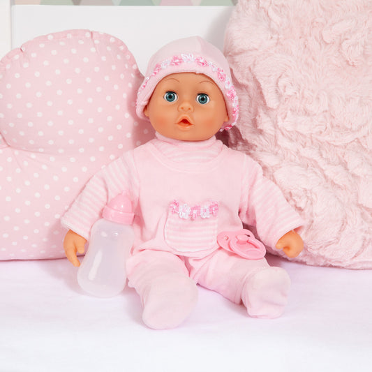 Pink baby doll wearing polka-dot bonnet and pink outfit with white bottle and pacifier, surrounded by pink textured blanket and pillow