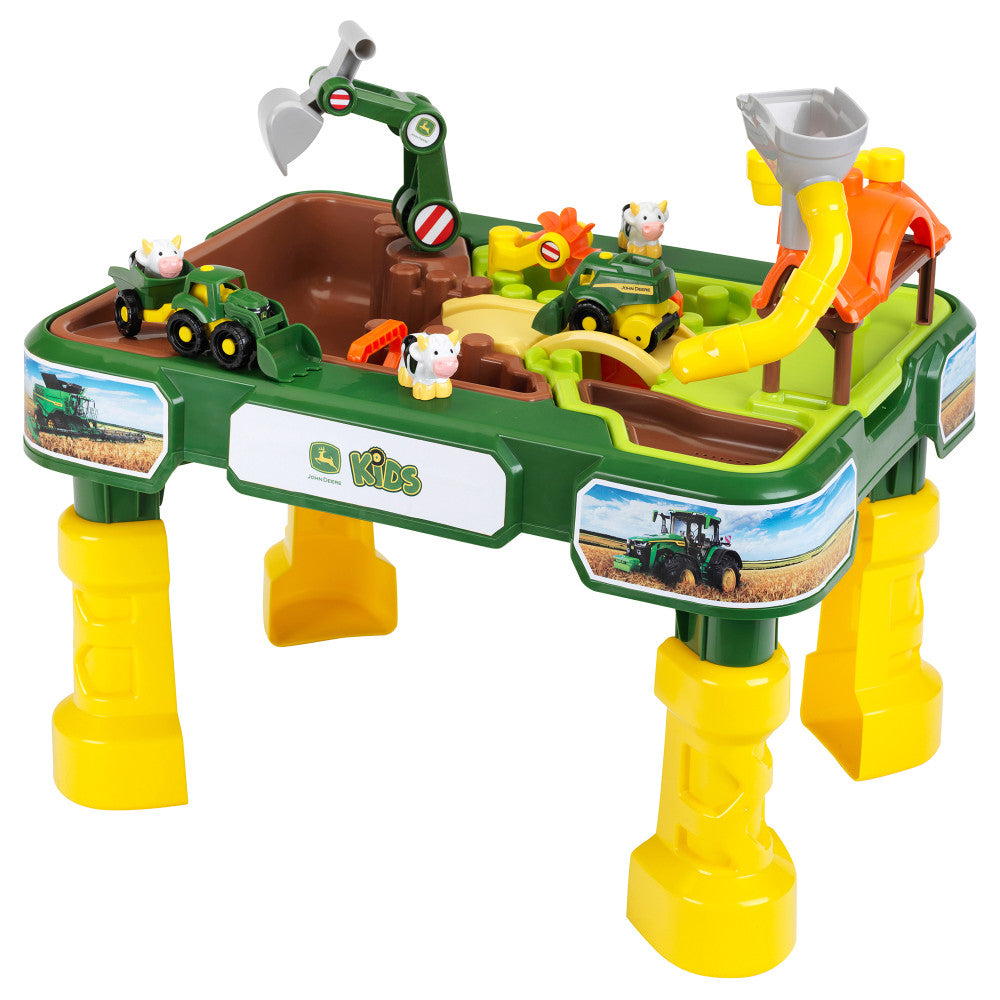John Deere green and yellow water table with brown sand pit, yellow slide, toy tractors, cows, and harvesting accessories on plain background