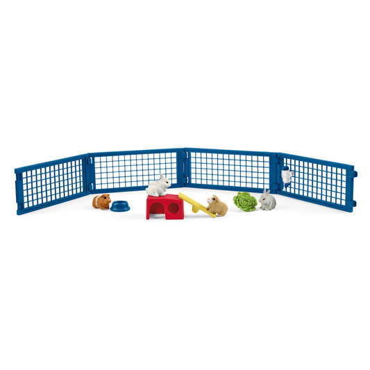 Blue folding play fence with small animal figurines including rabbits and guinea pigs, red house, yellow seesaw, blue bowl, and green lettuce piece on white bac