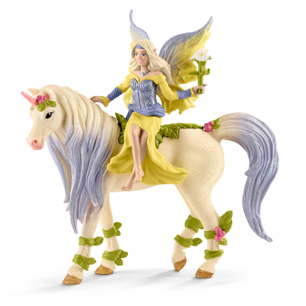 Fairy doll with blonde hair and yellow wings riding a cream unicorn with purple mane and tail, both decorated with green leaf and pink flower details