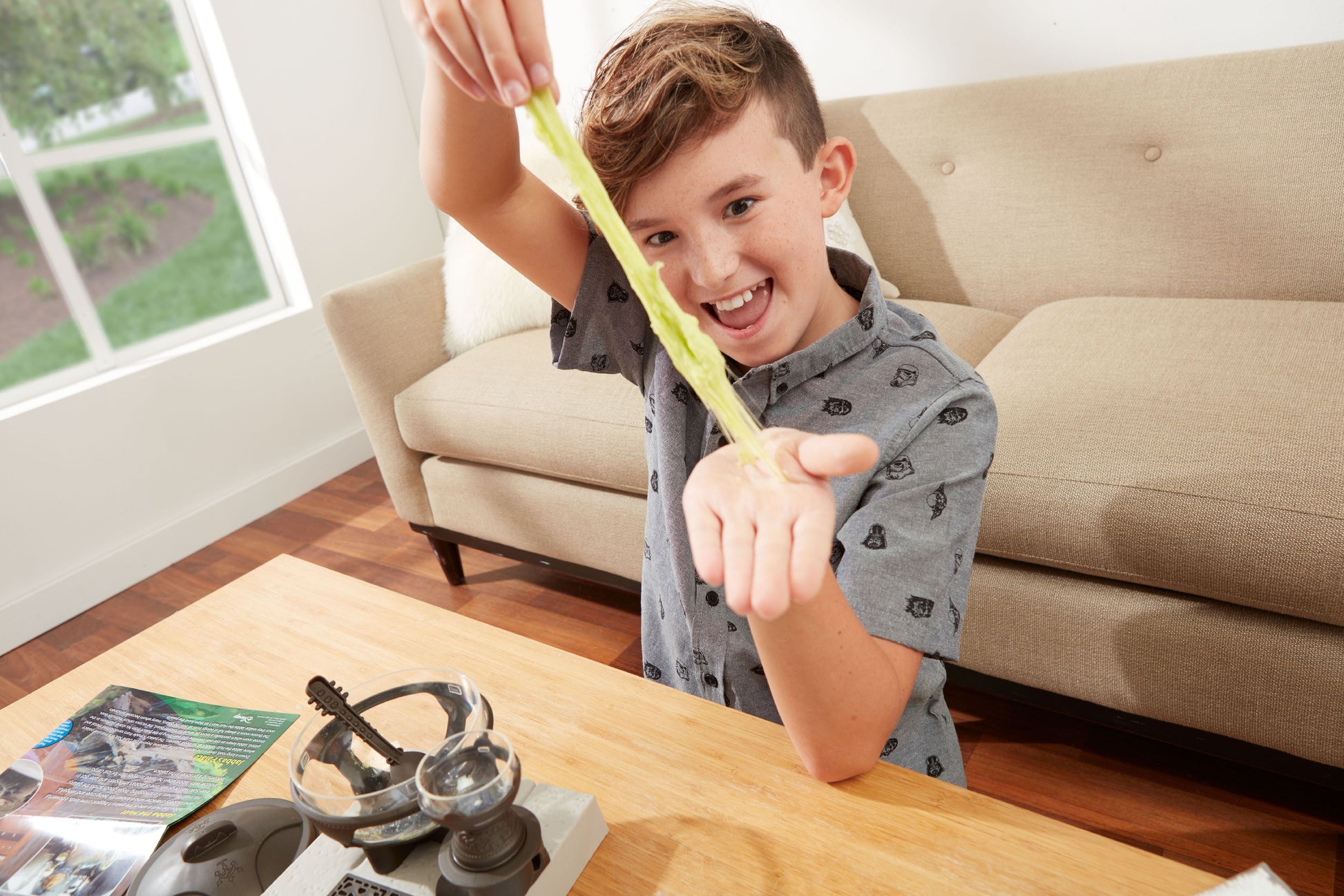 Child modeled by a child stretching yellow slime while sitting at a wooden table with Star Wars Jabba the Hutt Slime Lab kit and headphones