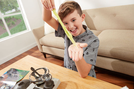 Child modeled by a child stretching yellow slime while sitting at a wooden table with Star Wars Jabba the Hutt Slime Lab kit and headphones