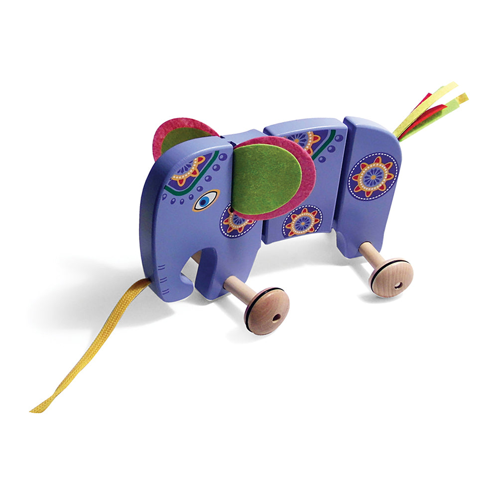 Purple wooden pull-along elephant toy with decorative orange and gold details, pink ears, wooden wheels, yellow pull string, and colorful ribbon tail