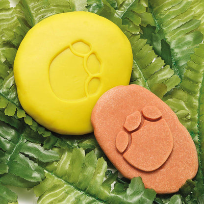 Dinosaur Footprint Fossils Discovery Set with yellow and orange fossil molds on green leaf background