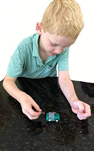 Child modeled by a boy examining a small turquoise circuit board or electronic component on a dark surface