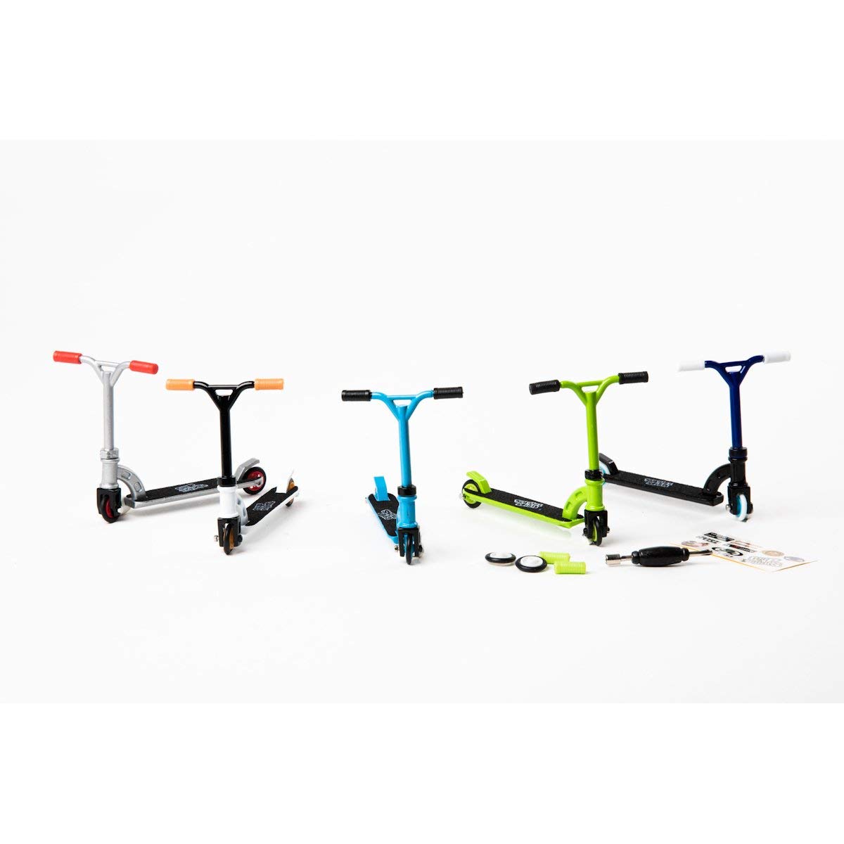 Five colorful finger scooters in silver, black, blue, green, and dark blue with handlebar grips, displayed with accessories including tools and instruction shee