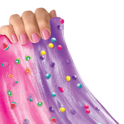 Hand with pink nail polish holding pink and purple slime with colorful beads, fruit charms, and mix-in decorations