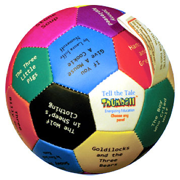 Colorful fabric ball with printed story prompts in multiple colors including pink, blue, green, yellow, black, and white panels; each panel shows text for story