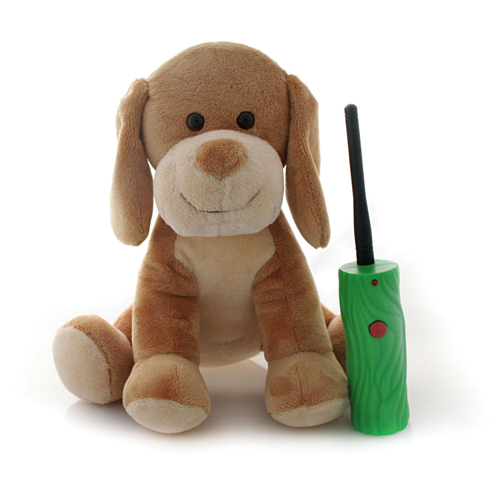 Tan and cream plush puppy toy with long floppy ears, black eyes, and embroidered smile, sitting next to a green interactive remote control with black antenna