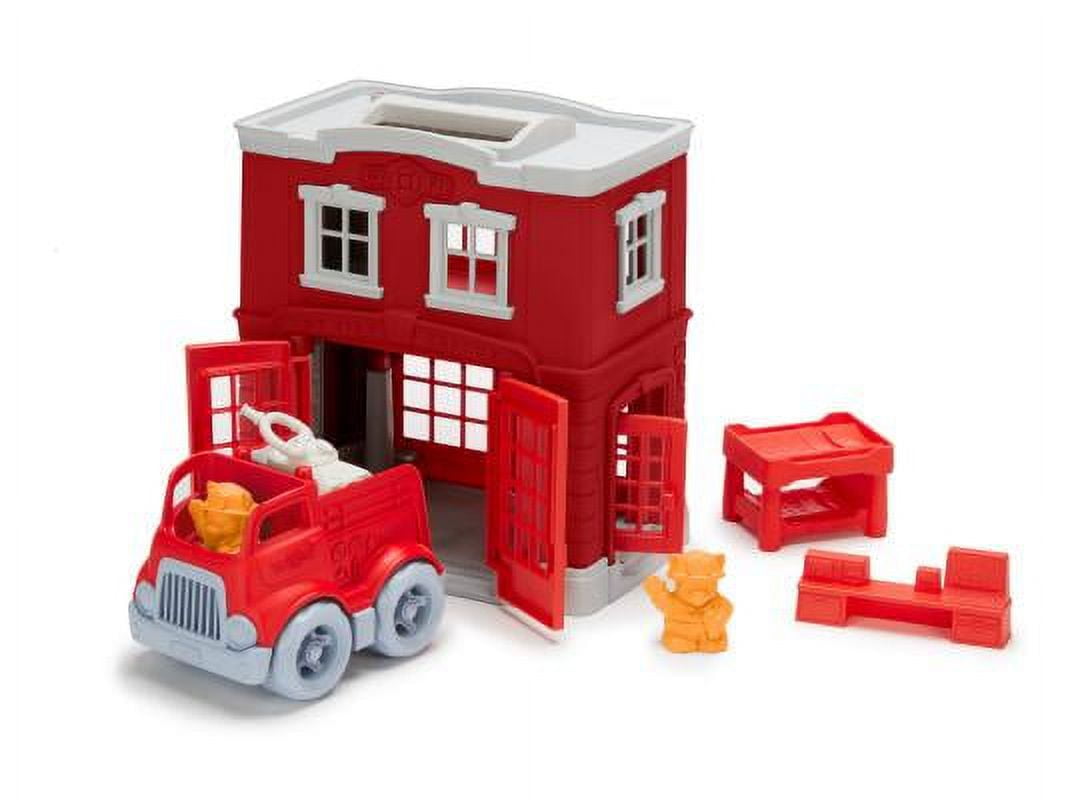 Red fire station playset with white-trimmed roof, opening doors, red fire truck with gray wheels, orange bear figure, and red accessory pieces