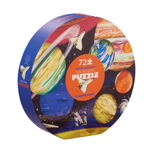 Crocodile Creek Solar System 72-piece jigsaw puzzle in round box featuring colorful illustrated planets, spacecraft, and stars against black space background