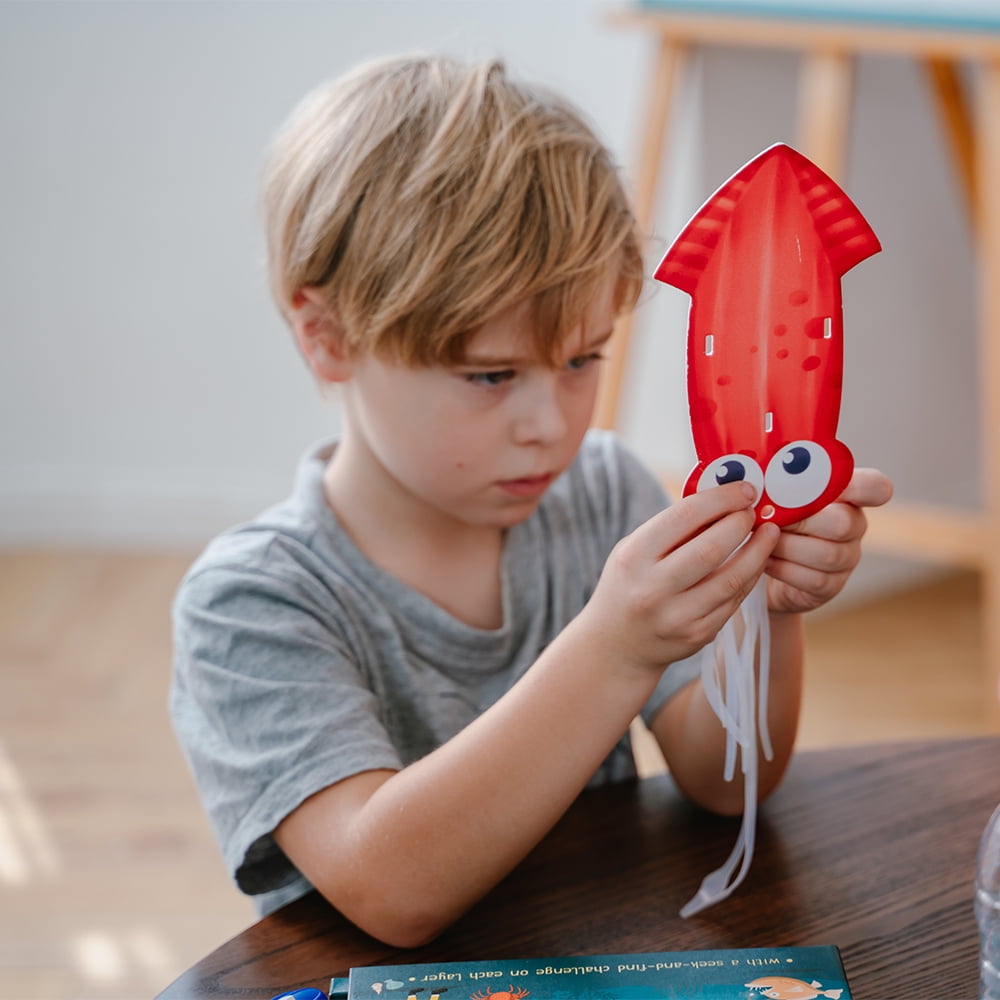 Red squid toy with googly eyes and tentacles, modeled by a child in gray shirt at wooden table