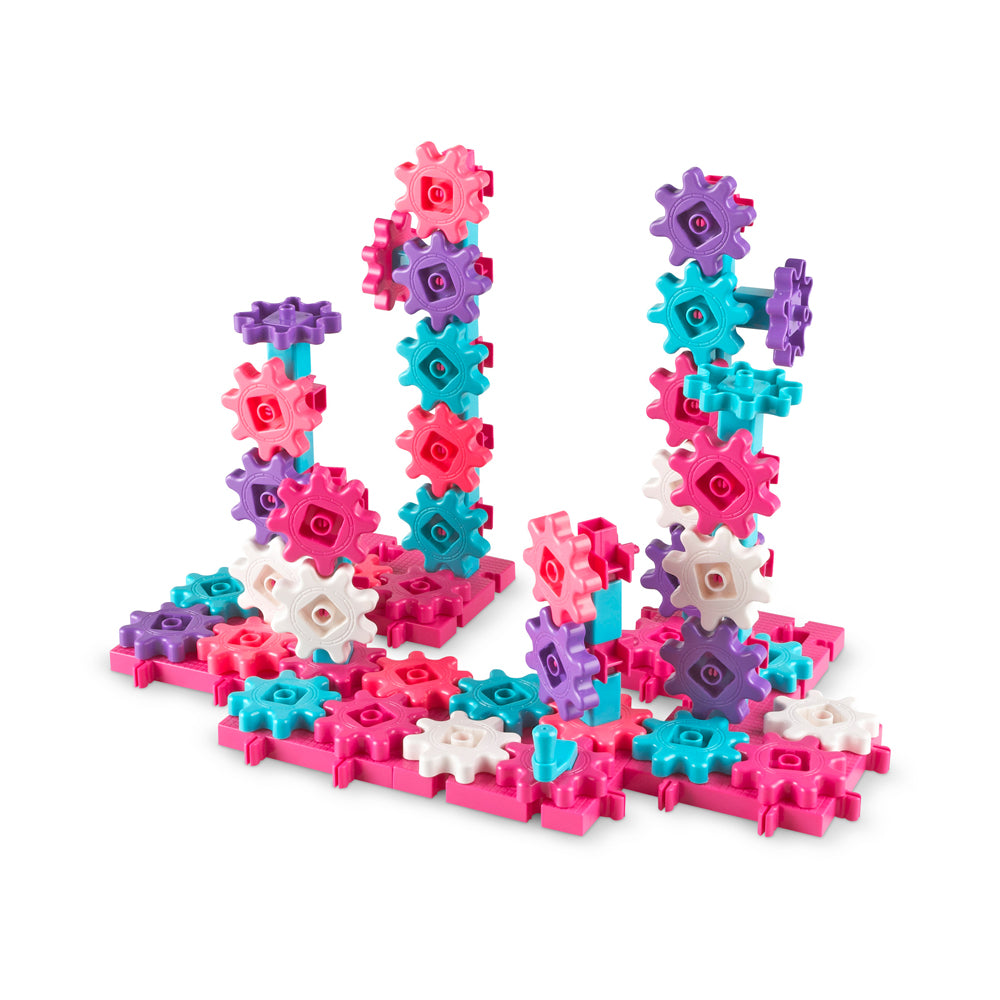 Colorful interlocking gears building set in pink, purple, turquoise, and white pieces assembled into three tall structures on a plain background