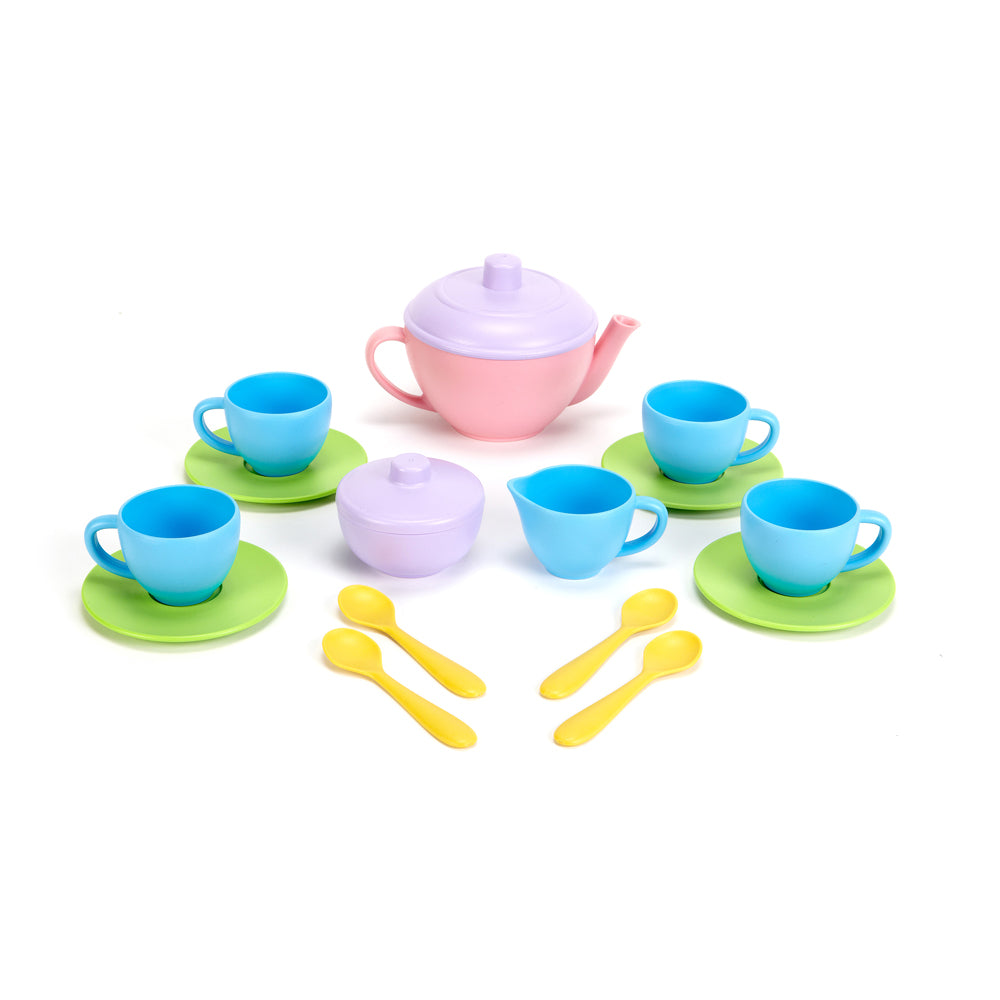Colorful plastic tea set with pink teapot, light blue cups on green saucers, purple sugar bowl, and yellow spoons arranged on white background