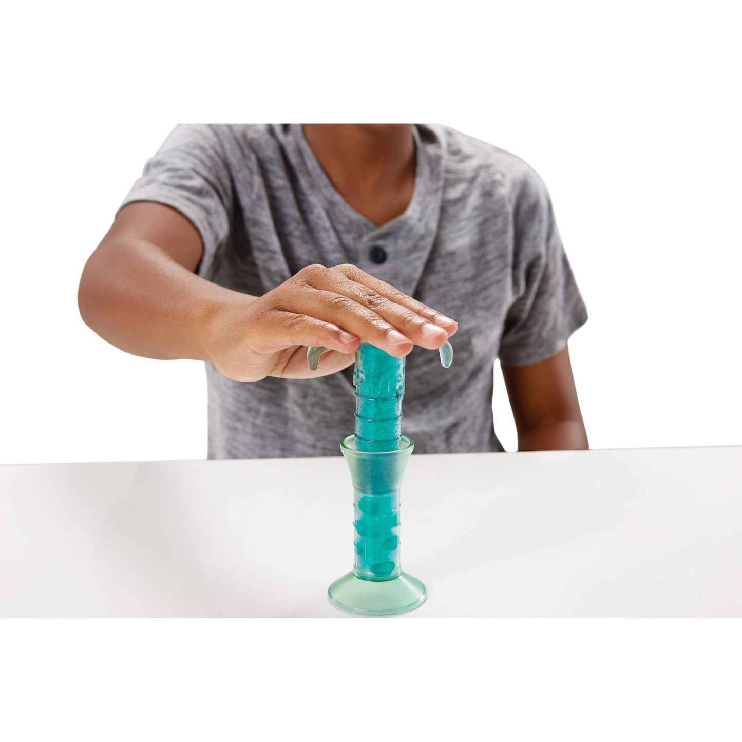 Child's hand stretching turquoise slime upward from a cup with clear base, modeled by a child