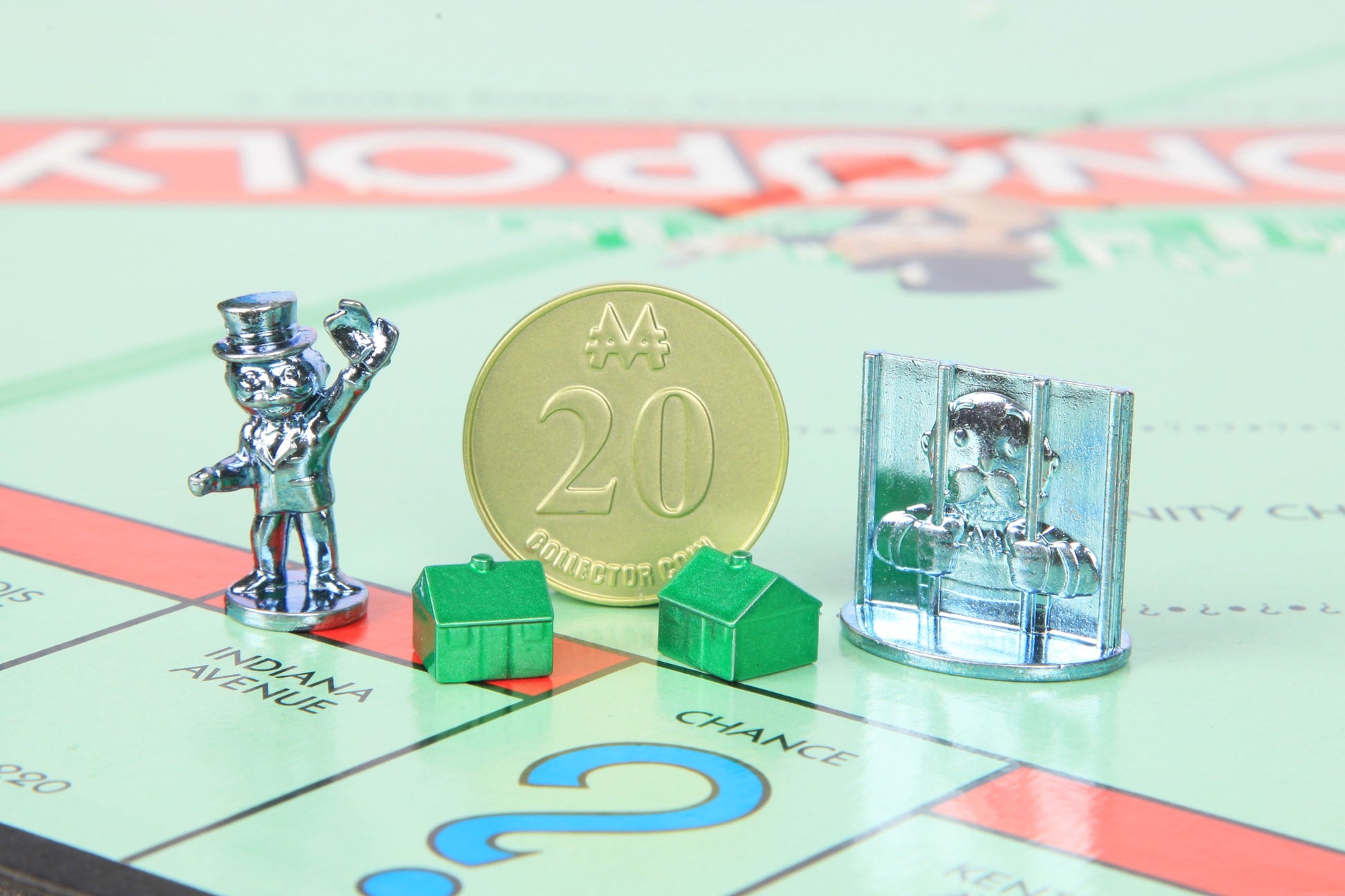 Monopoly game board with metal player tokens, gold collector coin marked 20, green plastic houses, and silver metal jail piece on light green properties