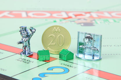 Monopoly game board with metal player tokens, gold collector coin marked 20, green plastic houses, and silver metal jail piece on light green properties