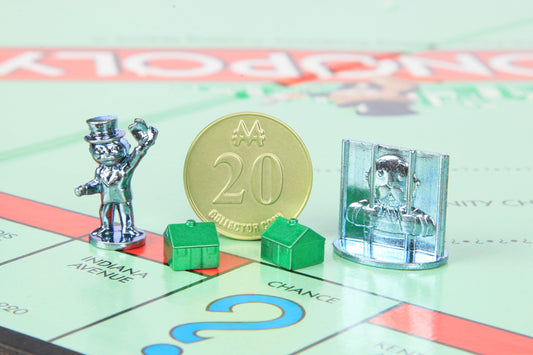Monopoly game board with metal player tokens, gold collector coin marked 20, green plastic houses, and silver metal jail piece on light green properties