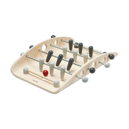 Wooden tabletop foosball game with light natural wood frame, metal rods, and black, white, and gray player pieces with one red ball