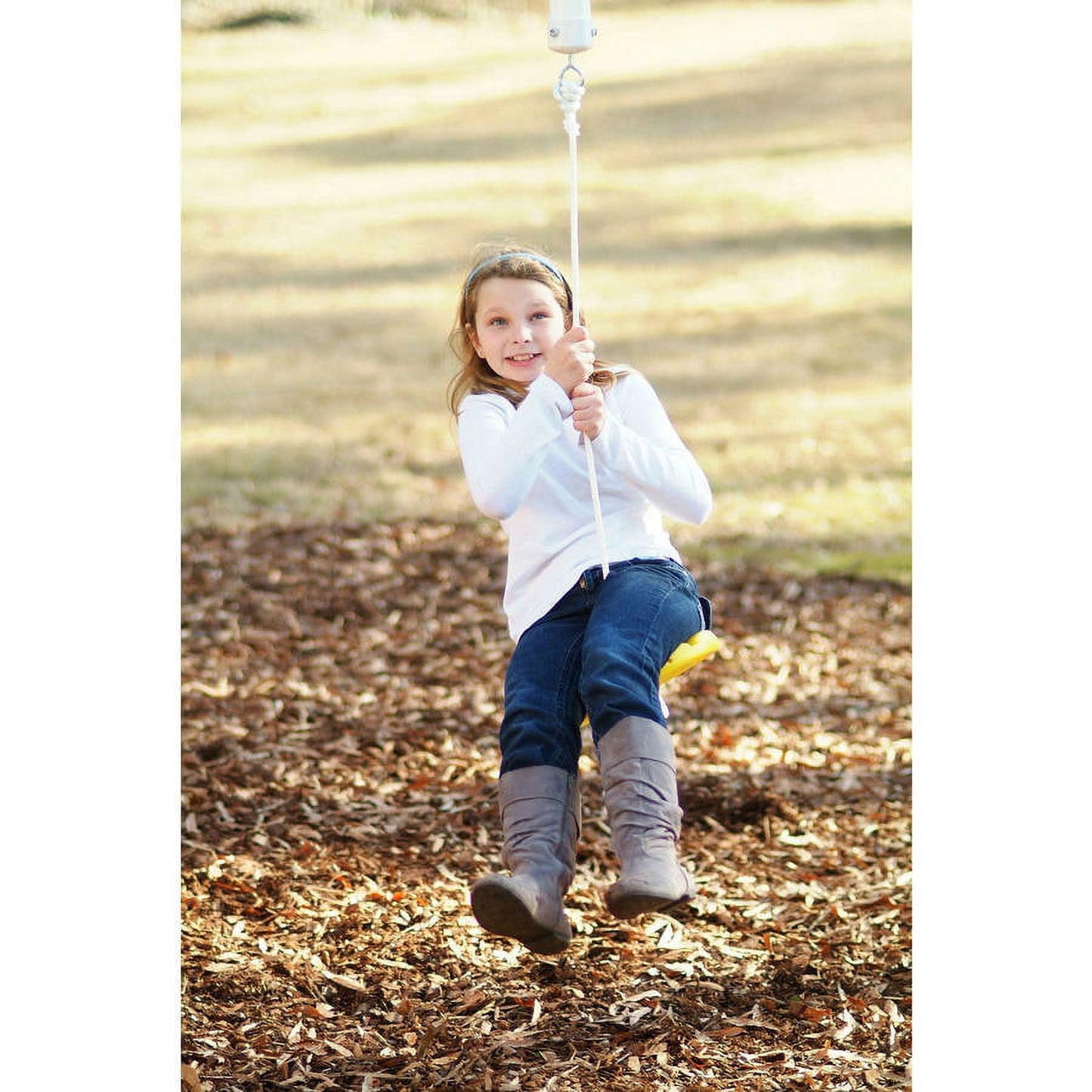 Child modeled by a girl on a rope swing suspended from an outdoor beam, swinging over a mulch ground area in a park setting