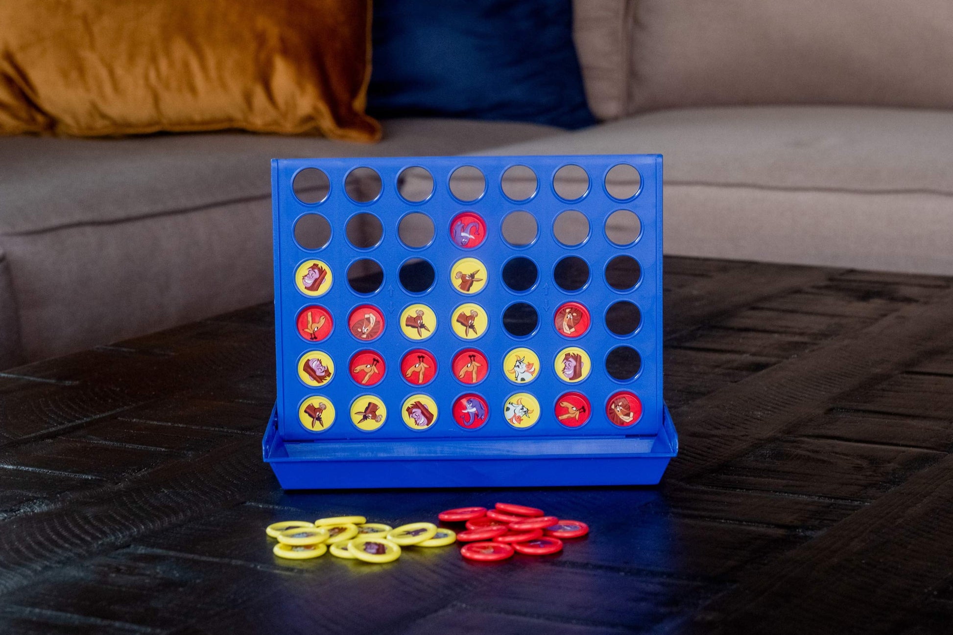 Connect 4 style game with blue plastic board featuring 42 holes filled with red and yellow game pieces showing character designs on a dark wooden surface