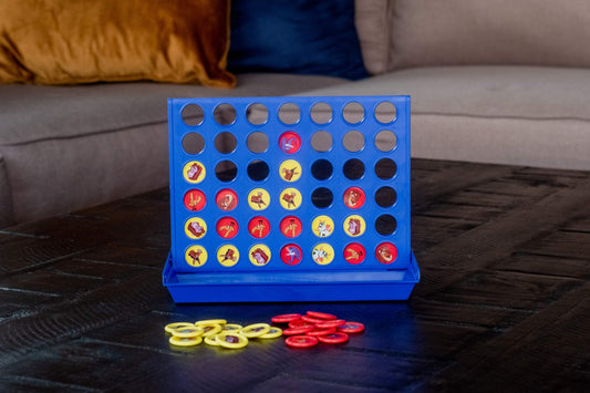 Connect 4 style game with blue plastic board featuring 42 holes filled with red and yellow game pieces showing character designs on a dark wooden surface