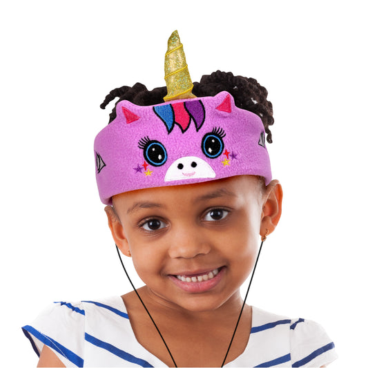 Pink fleece unicorn-shaped headband headphones with gold glitter horn, black curly mane, large blue eyes, and colorful mane details, modeled by a child
