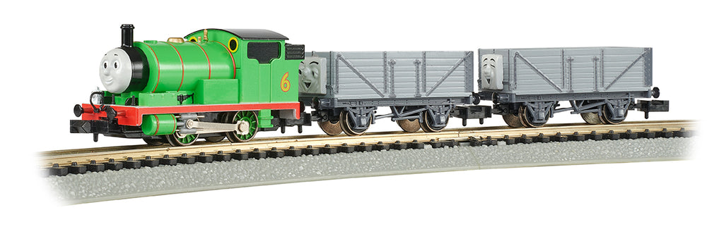 Green steam engine number 6 with red base pulling two gray freight cars on model train track
