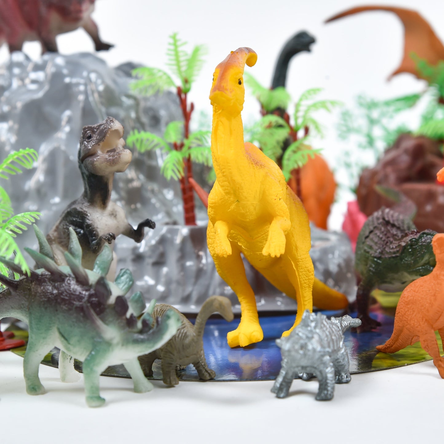 Yellow long-necked dinosaur figure displayed in a prehistoric scene with smaller dinosaurs, gray rock formations, green ferns, and orange dinosaurs on plain bac