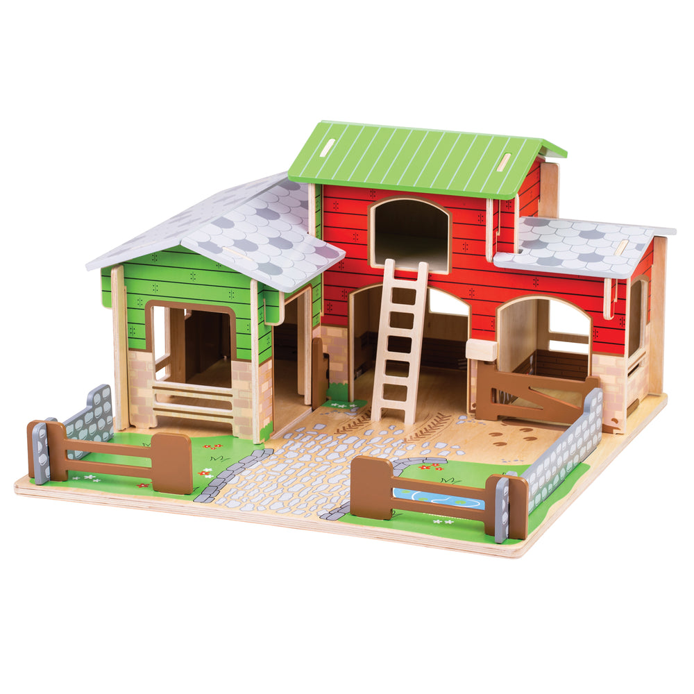 Wooden farm playset with green and red barn buildings, white-roofed structures, wooden ladder, fenced yard area, and natural wood base