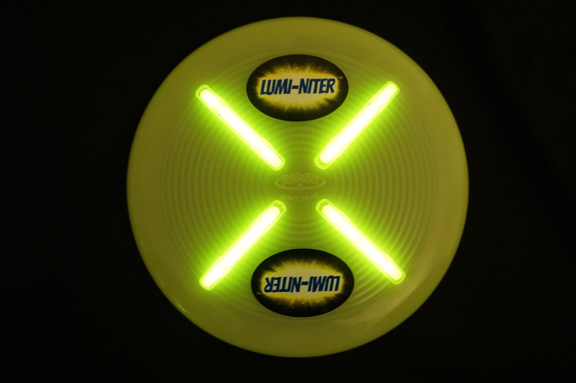 Lumi-niter yellow glow disc with bright green LED lights forming an X pattern, displayed against black background