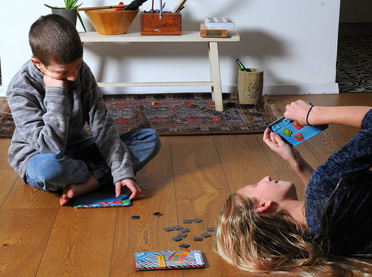 Two children playing Reversi magnetic travel game on wooden floor, with game pieces and boards displayed